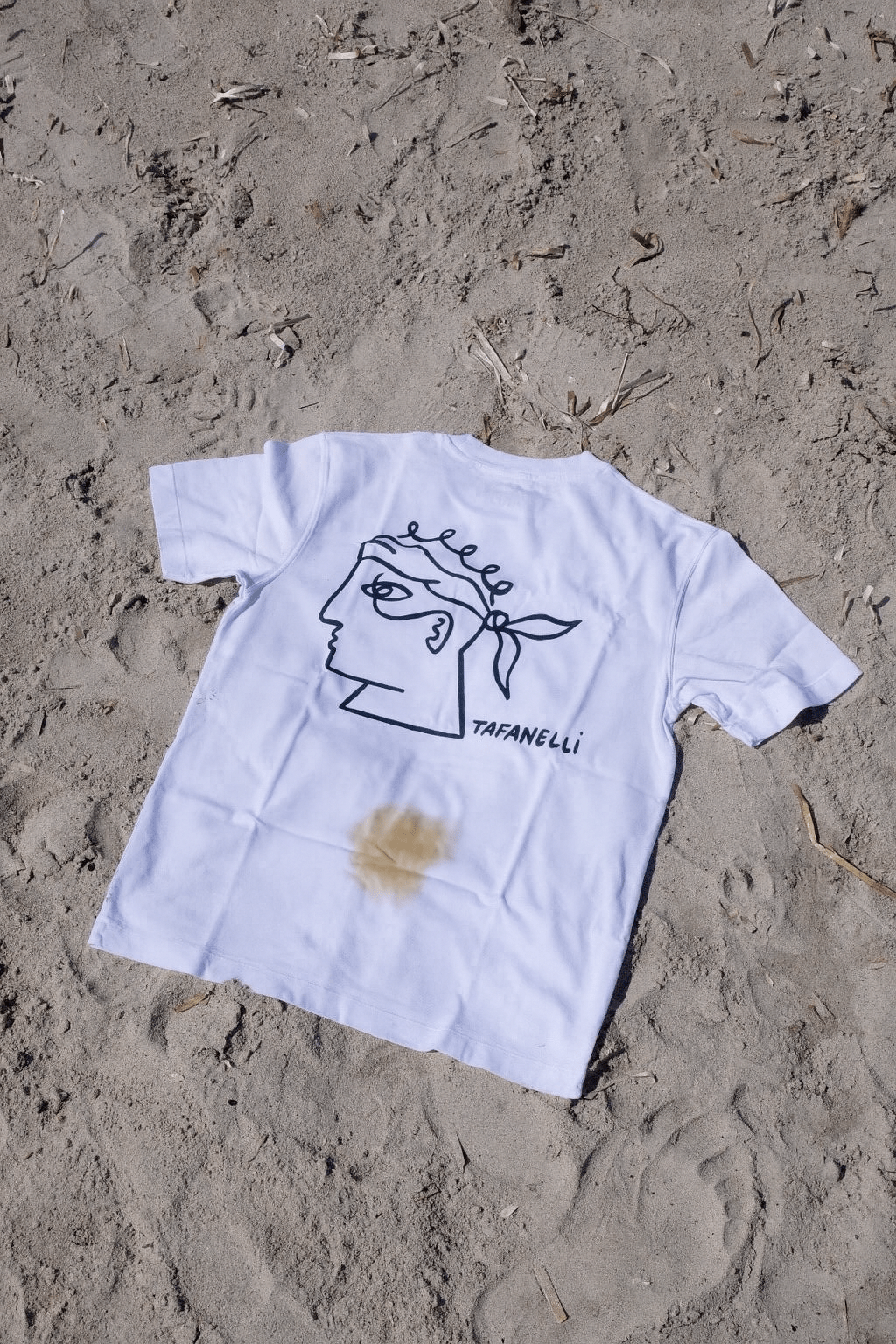 T-shirt Tafanelli en coton posé sur une table d’atelier, avec une main appliquant délicatement un savon doux pour retirer une tache.