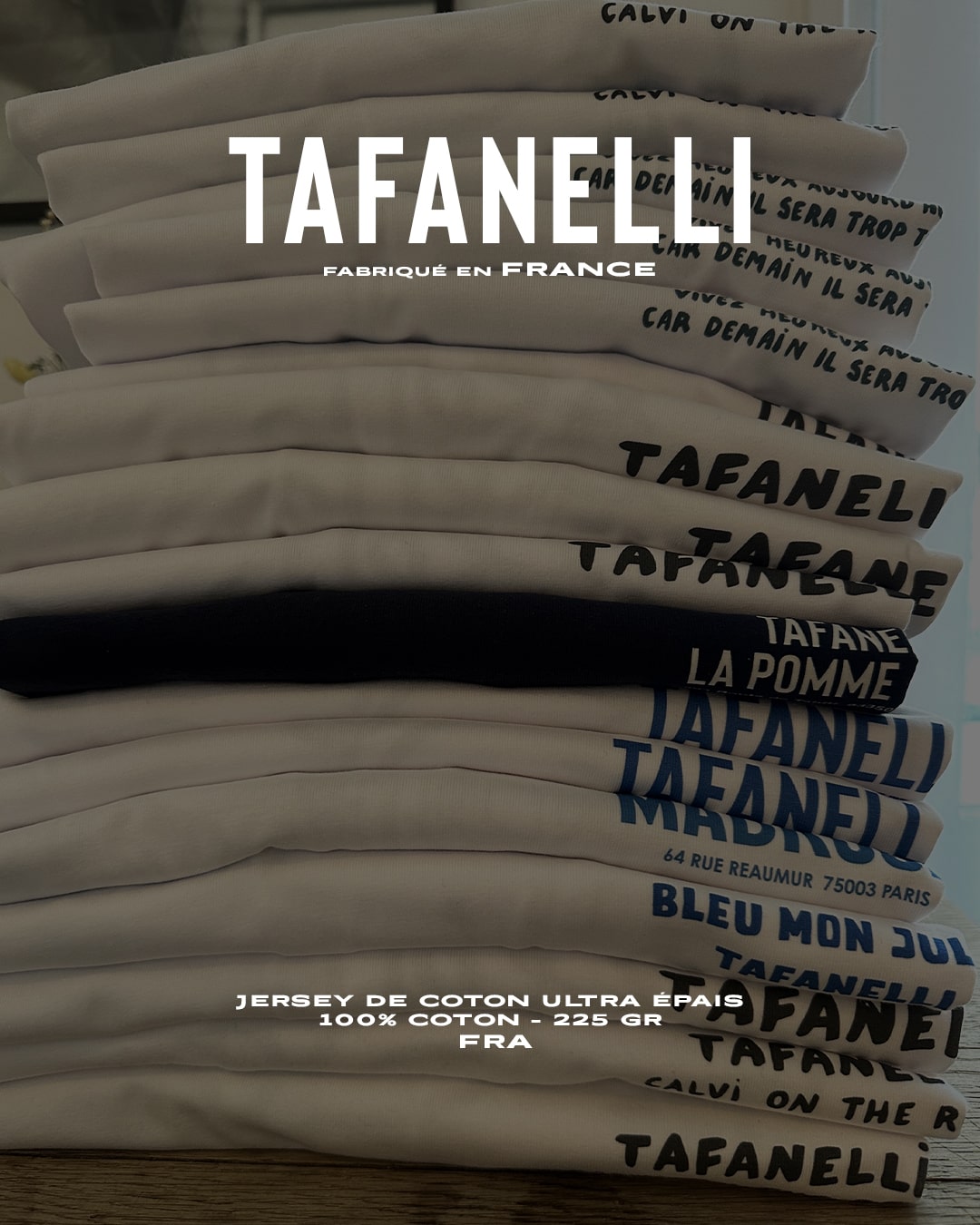 T-shirts Tafanelli soigneusement pliés sur une table d’atelier, lumière douce, coton dense et texture naturelle visible.